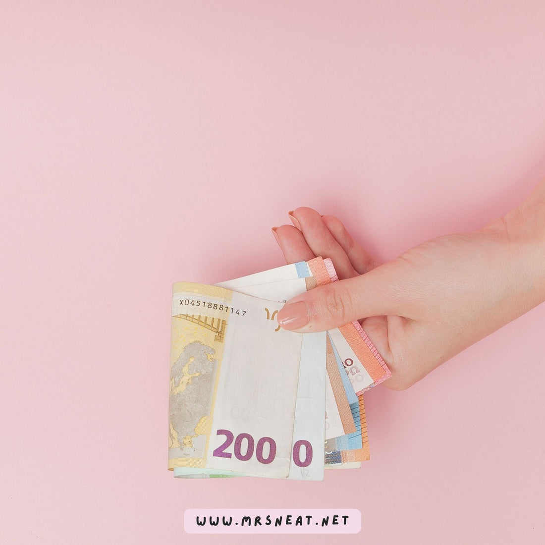 Hand holding cash against a soft pink background for a 50/30/20 budgeting guide