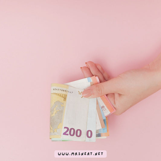Hand holding cash against a soft pink background for a 50/30/20 budgeting guide