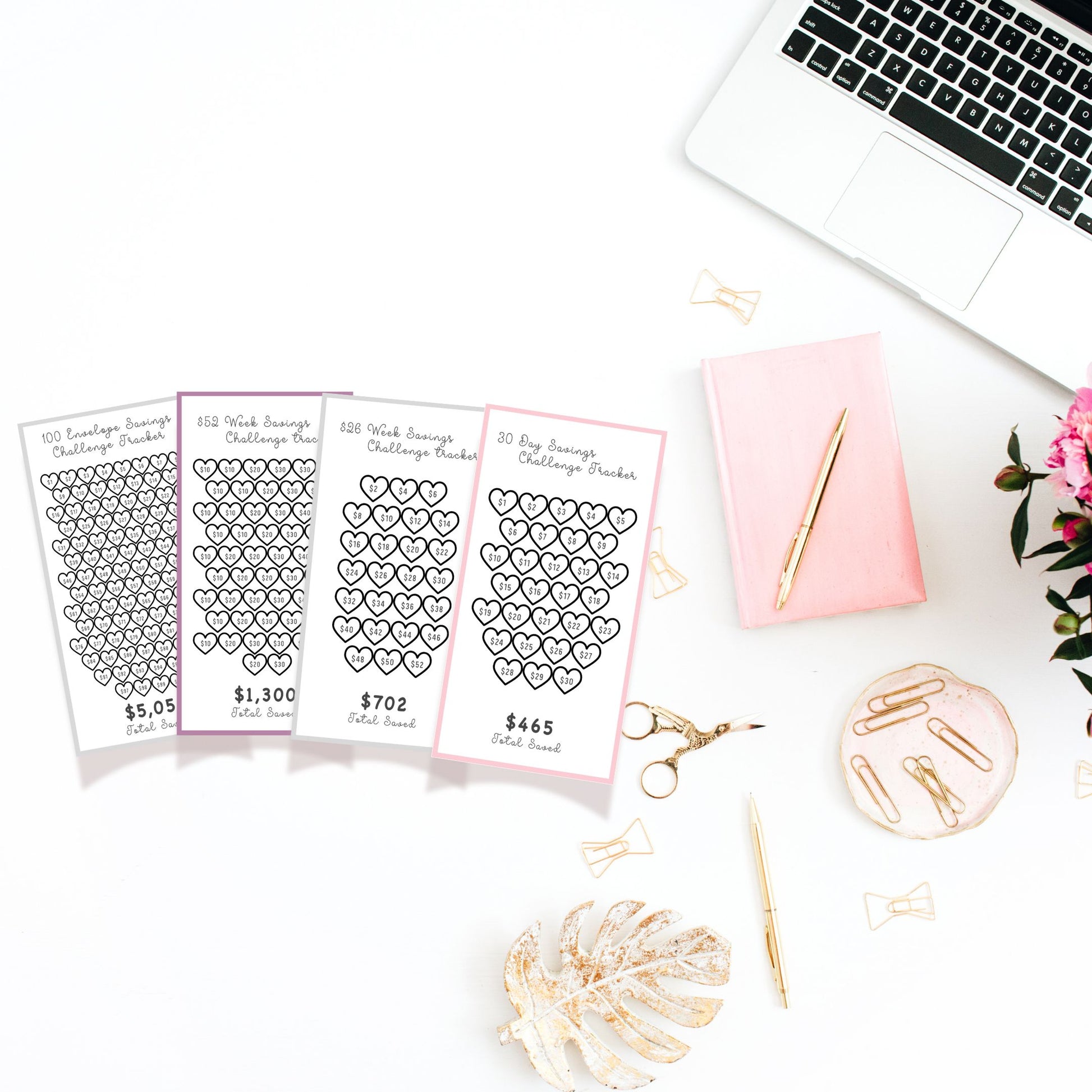 Heart-themed saving challenge charts on a desk with a laptop, pen, and decorative items.