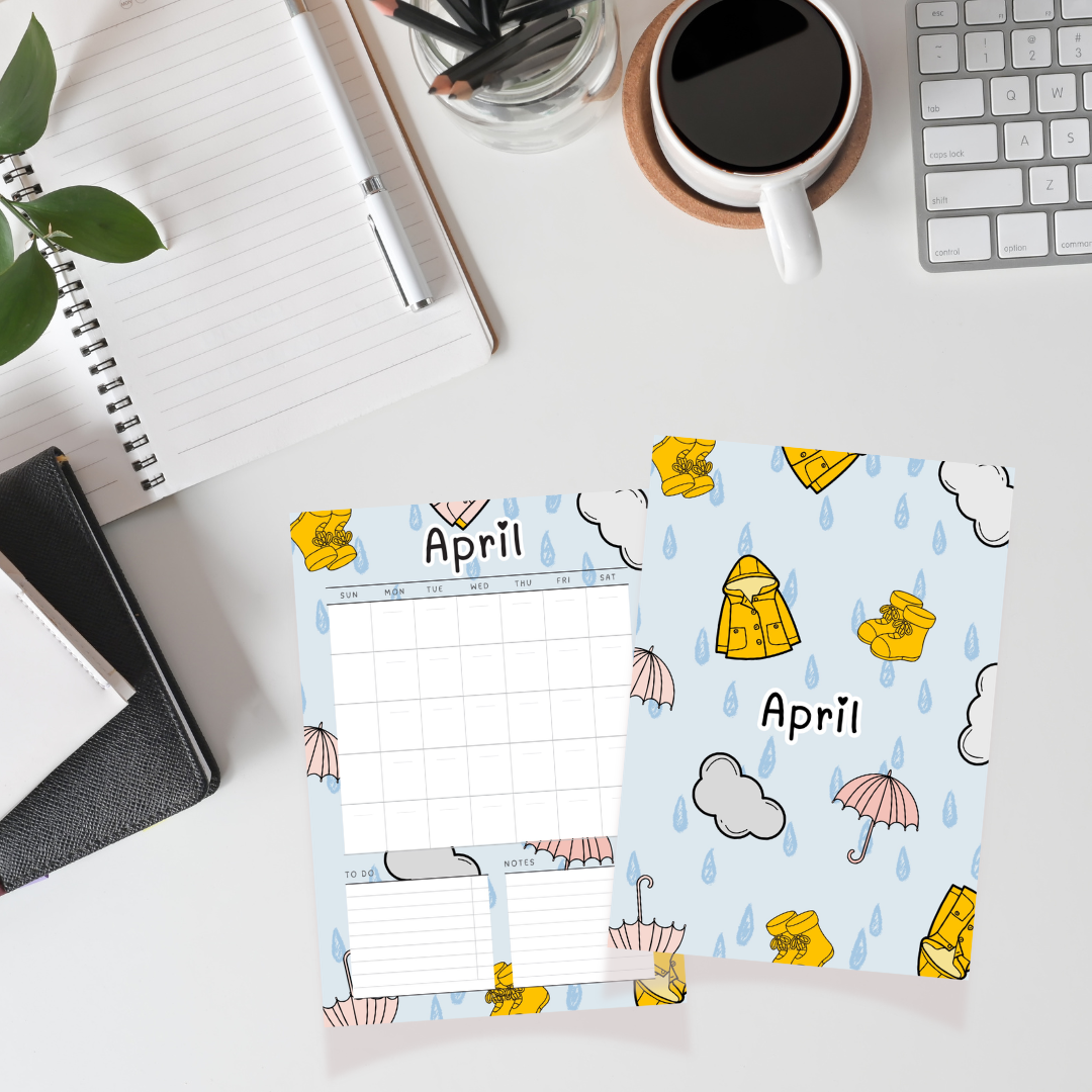April calendar with raincoat and umbrella design on a desk with coffee and stationery items.
